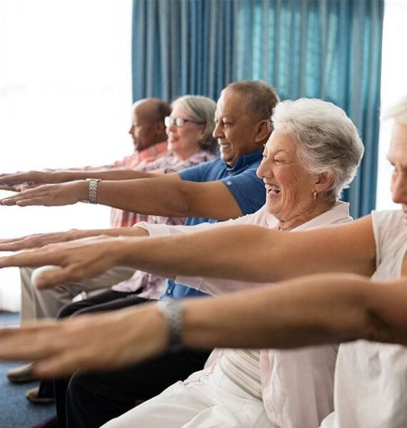 group of smiling people practising chair yoga with their arms stretched out